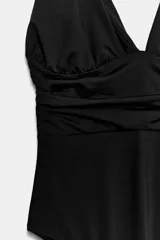 Body de poliamida color negro con escote en pico, tirantes anchos y detalle de tejido drapeado en la cintura. Presenta espalda abierta y cierre inferior con botones a presión.