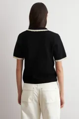 Sweater de punto negro de manga corta con cuello polo y ribetes contrastantes en color beige con detalles de encaje en el cuello y los puños.