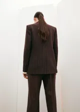 Blazer de corte sastrero en color marrón oscuro con diseño de rayas diplomáticas verticales. Presenta solapas clásicas, cierre frontal con botones y bolsillos laterales con solapa.