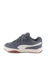Championes Puma modelo Park Lifestyle Sk8, de diseño urbano inspirados en el skate, color blanco con franja lateral negra, detalles en gamuza gris en la puntera y suela de goma marrón tipo gum.