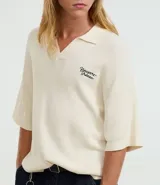 Camisa polo de hombre confeccionada en tejido de punto de algodón, color crema, con cuello en V y manga corta. Presenta un corte oversized y un pequeño bordado de lettering en el pecho.