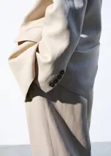 Blazer Paola de corte recto, color beige, confeccionado en mezcla de lana y lino. Presenta cuello pico con solapa, mangas largas, un bolsillo de ribete en el pecho, dos bolsillos con solapa en los laterales y cierre frontal de un botón oscuro.