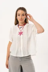 Blusa blanca de manga corta con cierre frontal de botones y detalle de pliegues verticales en la parte delantera. Presenta un corte recto y relajado, confeccionada en una tela liviana con textura.