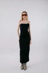 Vestido midi negro ajustado, con tirantes finos, escote recto y detalle de frunce en el lateral del busto. Presenta una abertura lateral en la falda.