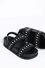Sandalia chunky de plataforma color negro, con diseño de doble tira ancha decorada con tachas metálicas cónicas y pulsera ajustable al tobillo con hebilla.