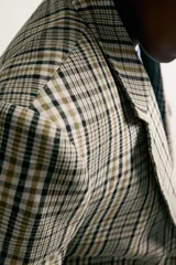 Blazer de corte boxy fit de Zara, confeccionado en tejido con algodón con estampado a cuadros en tonos beige, negro y blanco. Cuenta con cuello de solapas de muesca, manga larga con botones en los puños, bolsillos de vivo en el pecho y de plastrón en la cadera, y cierre frontal con un botón.