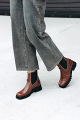 Bota tipo Chelsea de cuero color marrón, con paneles laterales elásticos en color negro y suela track robusta de goma negra.