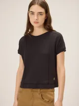 Remera tejida color beige de corte relajado, con mangas cortas y detalle de costuras frontales marcadas. Incluye un pequeño bordado distintivo en el borde inferior.