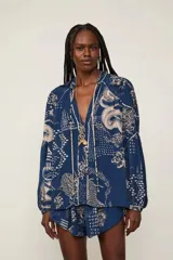 Blusa oversize azul con estampado integral en tonos claros, cuello en V con cordones ajustables, mangas largas abullonadas y puños elásticos.