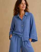 Camisa de lino color azul jean, con cuello camisero, cierre frontal con botones y mangas largas anchas con detalle de pliegues en los puños.
