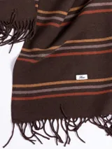 Bufanda de tejido suave en color marrón chocolate con diseño de rayas horizontales en tonos naranja, beige y gris. Presenta terminaciones con flecos en los extremos.