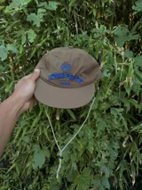 Gorra de color marrón claro con visera curva y logo bordado en azul claro en el frente.