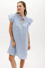 Vestido corto celeste de lino, corte suelto, con cuello redondo con volados y lazo, mangas cortas con volados.
