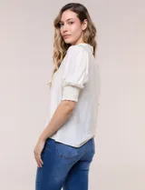 Blusa blanca de crepé con cuello mao y escote en V, cierre frontal con botones, mangas cortas abullonadas con puños elastizados en punto smock y calce semi holgado.