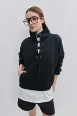 Buzo de algodón negro con calce relajado, cuello alto con cordones cruzados y ojales metálicos, bolsillos laterales y puños y ruedo elásticos.