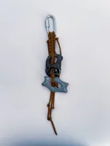 Charm para bolso o accesorios con mosquetón metálico, tejido de macramé en cordón negro y dijes de cerámica esmaltada en tonos violeta y celeste.
