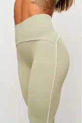 Calza deportiva de tiro alto color verde claro, con costuras laterales en contraste de color blanco que recorren la prenda desde la cintura hasta los tobillos.