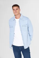 Camisa de jean celeste de manga larga, con cuello clásico, cierre frontal con botones a presión, dos bolsillos con solapa abotonada en el pecho, corte en hombros y detalle en la espalda.