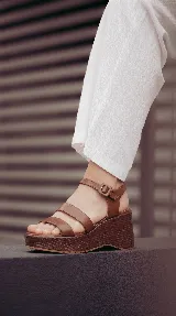 Sandalia de cuero marrón con plataforma corrida y taco alto texturizado. Posee tiras delanteras múltiples y una pulsera al tobillo con hebilla ajustable.