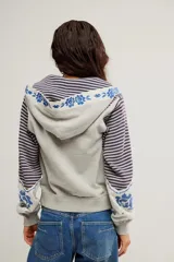 Buzo con capucha y cierre frontal de cremallera, confeccionado en tejido de punto rayado en tonos gris y azul, combinado con paneles lisos y detalles de estampado floral en la capucha y los puños. Presenta bolsillos frontales estilo canguro y diseño de largo corto.