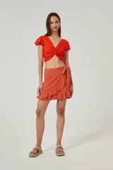 Minifalda color terracota de diseño cruzado, con lazo lateral para atar y volados en el borde delantero y en el ruedo.