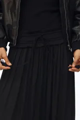 Pollera maxi negra de corte holgado, confeccionada con cintura elástica fruncida y cordón ajustable con borlas colgantes.