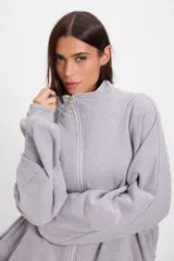 Campera holgada de felpa color gris, con cuello alto, cierre frontal completo, mangas tipo murciélago y bolsillos laterales.