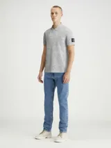 Chomba gris jaspeado de piqué de algodón peinado, con cuello clásico y tapeta de dos botones. Tiene mangas cortas, dobladillo con aberturas laterales y logo de Calvin Klein en la manga.