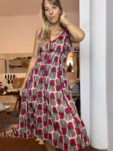 Vestido de verano con tirantes finos, escote en V ribeteado en color vino, y falda amplia con vuelo. Presenta un estampado repetitivo con formas abstractas en tonos beige, marrón oscuro y fucsia/vino.