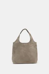 Bolso mini shopper de gamuza color marrón, con doble asa de mano y asa bandolera extraíble. Cuenta con cierre mediante botón imantado y bolsillo interior con cremallera.