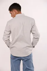 Camisa de manga larga en color gris, confeccionada en algodón, con cuello abotonado y cierre frontal de botones.