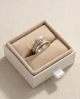 Anillo ancho de acero con baño de oro, compuesto por múltiples bandas texturizadas y una banda central engastada con circonias brillantes.