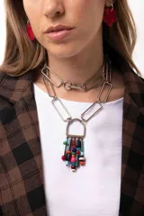 Collar de cadena con eslabones rectangulares plateados, diseñado para usarse largo o doble como gargantilla. Presenta un dije central en forma de herradura del cual cuelgan múltiples cuentas de diversos colores, formas y materiales.