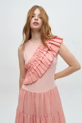 Vestido largo color salmón, con cuerpo ajustado de algodón y falda amplia de rayon, nylon, poliéster y elastano. Presenta un volante plisado en diagonal desde el hombro hasta la cintura.