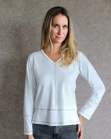 Remera blanca de manga larga con cuello en V, destacada por costuras decorativas en color contrastante que recorren el centro, el ruedo y los puños.