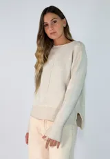 Sweater de punto color beige, con cuello redondo, manga larga con puños acampanados y diseño con tajos laterales en el ruedo, siendo más largo en la parte posterior.