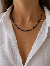Collar de cuentas facetadas negras con cierre y cadena de alargue dorada, finalizada con un pequeño dije en forma de corazón.
