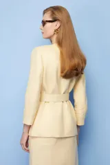 Blazer amarillo con solapas, corte entallado, cierre cruzado con botón y cinturón con hebilla redonda.