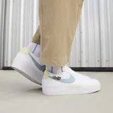 Championes Nike Blazer Low Platform Next Nature, de diseño bajo con plataforma. Presentan un cuerpo de lona blanca con detalles en cuero texturizado, un swoosh lateral en color celeste y un pequeño parche bordado decorativo. Incluyen refuerzos en la puntera y el talón en tonos neutros.