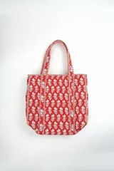 Bolso tipo tote bag acolchado, de color rojo con estampado floral en tonos blancos, con doble asa de hombro y detalles de costuras a rayas.