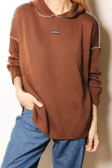 Sweater de punto color marrón con capucha, diseño holgado y costuras a la vista con pespunte a contratono. Presenta etiqueta con logo en el centro del pecho.