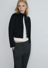 Chaqueta corta de diseño recto, color negro, con cuello de tira, cierre frontal con cremallera, bolsillos laterales y un bolsillo de ribete en el pecho.