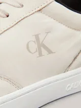 Zapatillas de corte bajo Calvin Klein Jeans en color beige, confeccionadas en una combinación de ante y piel nobuck. Presentan un diseño minimalista con suela cupsole blanca, detalle de trabilla trasera en color marrón y forro interior en contraste negro. Incluye el logo de la marca grabado en el lateral y en la mediasuela.