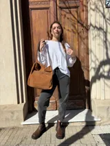 Cartera tipo tote bag de cuero color camel, con detalles de tachas metálicas en el bolsillo frontal y tiras largas para el hombro.