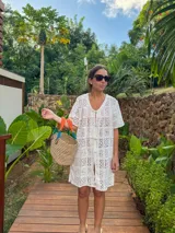 Vestido corto color blanco, tejido calado tipo encaje de algodón, corte recto y suelto, con mangas cortas, botonadura frontal forrada y escote en V.