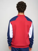 Buzo de felpa con diseño de bloques de color, predominantemente rojo en el cuerpo y azul marino en las mangas y hombros. Presenta el escudo del Club Nacional de Football y el logo de Umbro en el pecho.