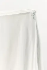Falda midi de tiro medio, color blanco, confeccionada en hilatura de viscosa 100%, con detalle de aplicación de tejido combinado semitransparente con abertura en el bajo y cierre lateral con cremallera oculta.