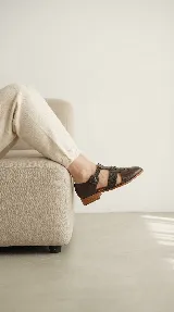 Zapato tipo cangrejera de cuero color marrón oscuro, con diseño de tiras entrelazadas, pulsera con hebilla ajustable al tobillo y taco bajo de madera.