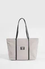 Cartera tipo shopper color beige con asas y detalles decorativos en cuero sintético negro. Cuenta con un bolsillo frontal exterior adornado con una etiqueta rectangular de la marca Symphorine.