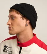 Gorro tipo fisherman de tejido acrílico con textura acanalada, diseño corto y etiqueta pequeña con logo en el frente.